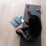 A woman stretching while looking at VeSync next to the Etekcity HR Smart Fitness Scale