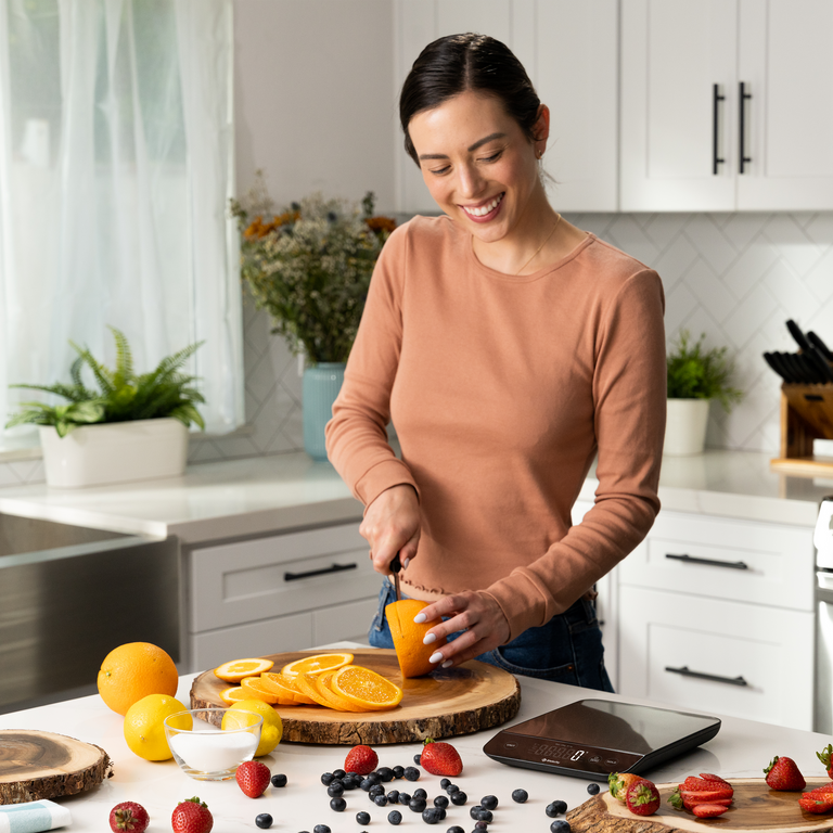 A woman chopping ingredients next to the Etekcity Luminary™ Kitchen Scale 